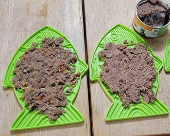 two of the green fish shaped lick mats covered in wet food