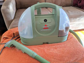 Bissell Little Green portable carpet cleaner on an orange towel, designed for quick and efficient stain removal in home cleaning tasks