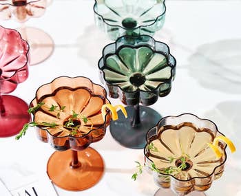 Six decorative glass cocktail cups with herbs and lemon garnishes on a table, next to a magazine and a 2023 award emblem