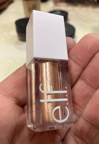 A hand holds an e.l.f. Cosmetics liquid glitter eyeshadow in a compact, rectangular bottle