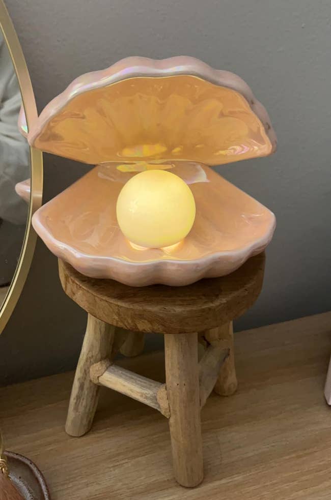 Glowing pearl-shaped light inside a clam shell lamp on a wooden stool