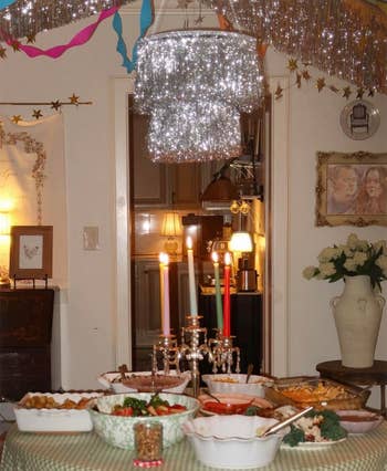 A table with various dishes and a candelabra, set under a glittery, festive chandelier. Streamers and stars adorn the room for a celebration