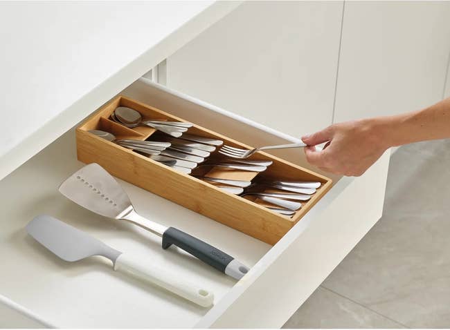 Hand places cutlery in a bamboo organizer inside a drawer, showcasing an efficient kitchen storage solution