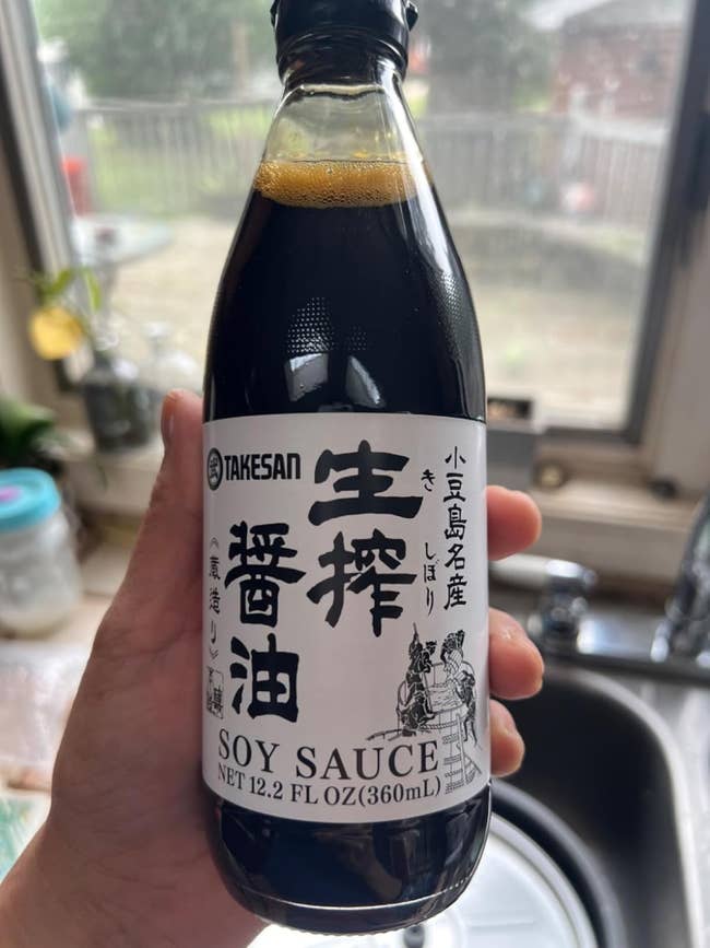 Hand holding a 12.2 fl oz bottle of Takesan soy sauce