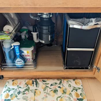 Under-sink organizer with cleaning supplies and trash bin, featuring pull-out baskets for efficient storage in a kitchen cabinet