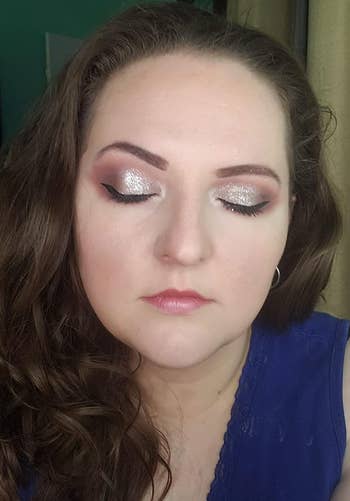 Close-up of a person with wavy hair, wearing shimmery eye makeup and closed eyes, dressed in a sleeveless top