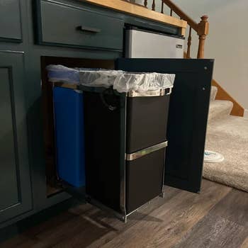 Pull-out kitchen cabinet trash and recycling bins, partially extended on a metal track