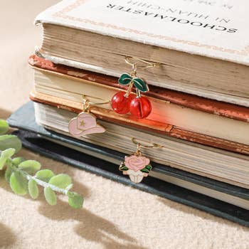 Gold rings with cherry, cap, and rose charms are displayed on vintage books