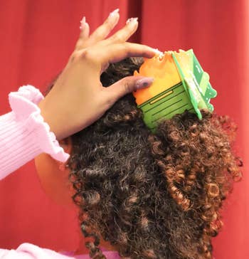 A person styles their curly hair with a colorful, geometric hair clip, showcasing a playful fashion accessory for a shopping article