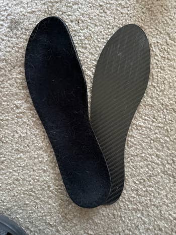 Two shoe insoles, one textured and one smooth, placed on a carpet