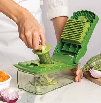 Person using a vegetable slicer to cut a zucchini on a kitchen counter