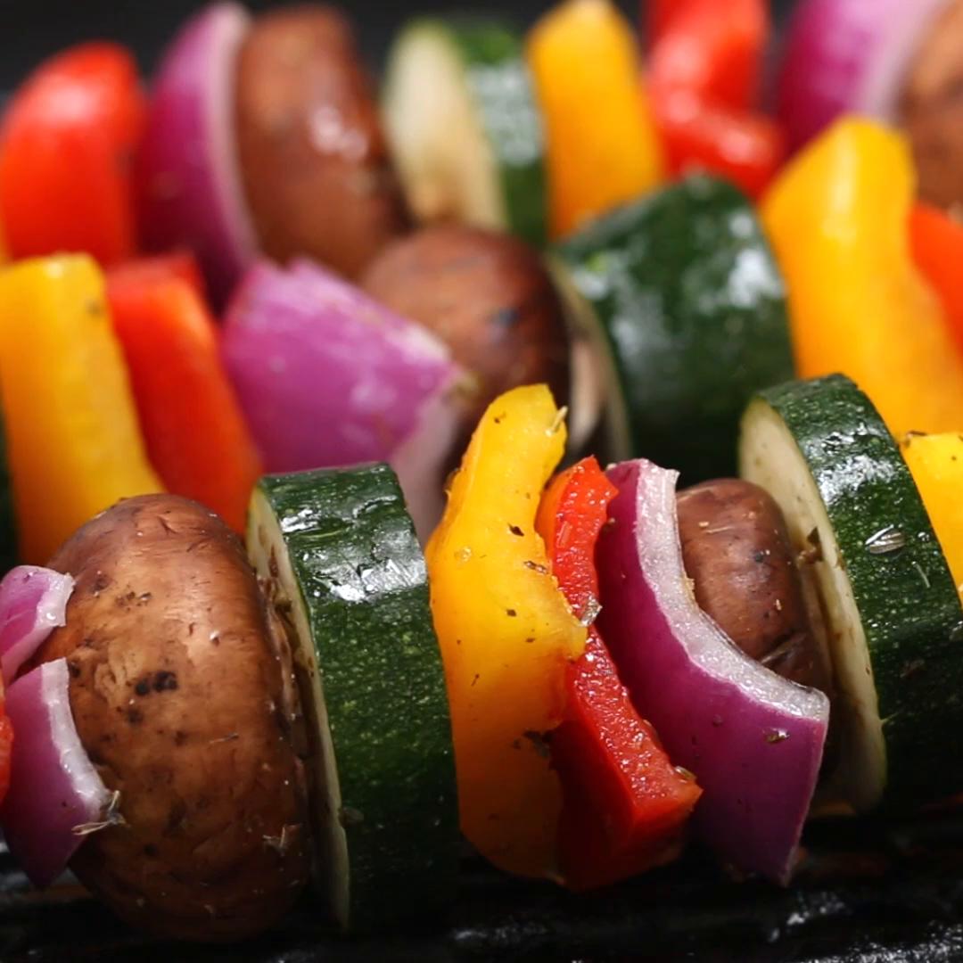 Grilled vegetable skewers with mushrooms, zucchini, red onions, and bell peppers arranged closely on a grill