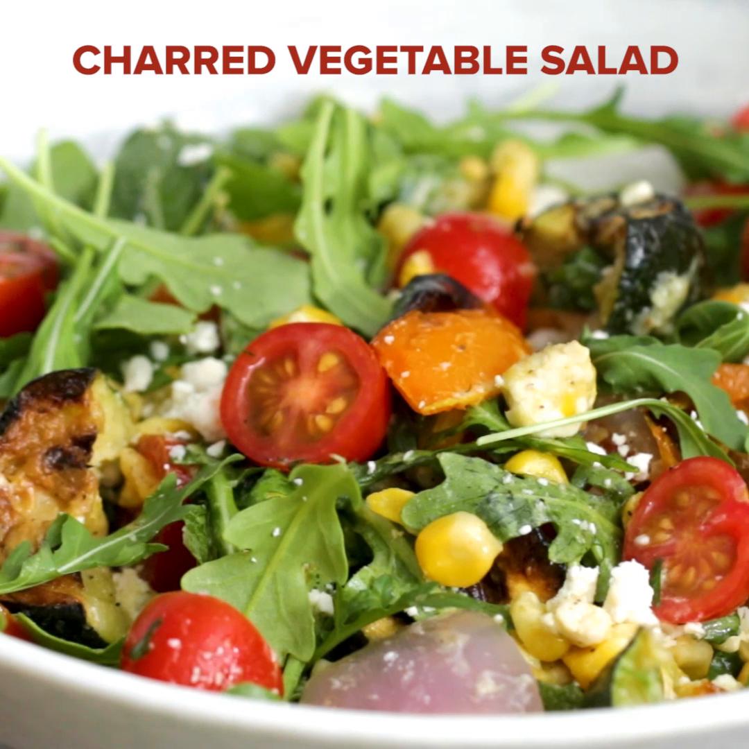 Charred vegetable salad with arugula, cherry tomatoes, corn, and feta cheese in a white bowl