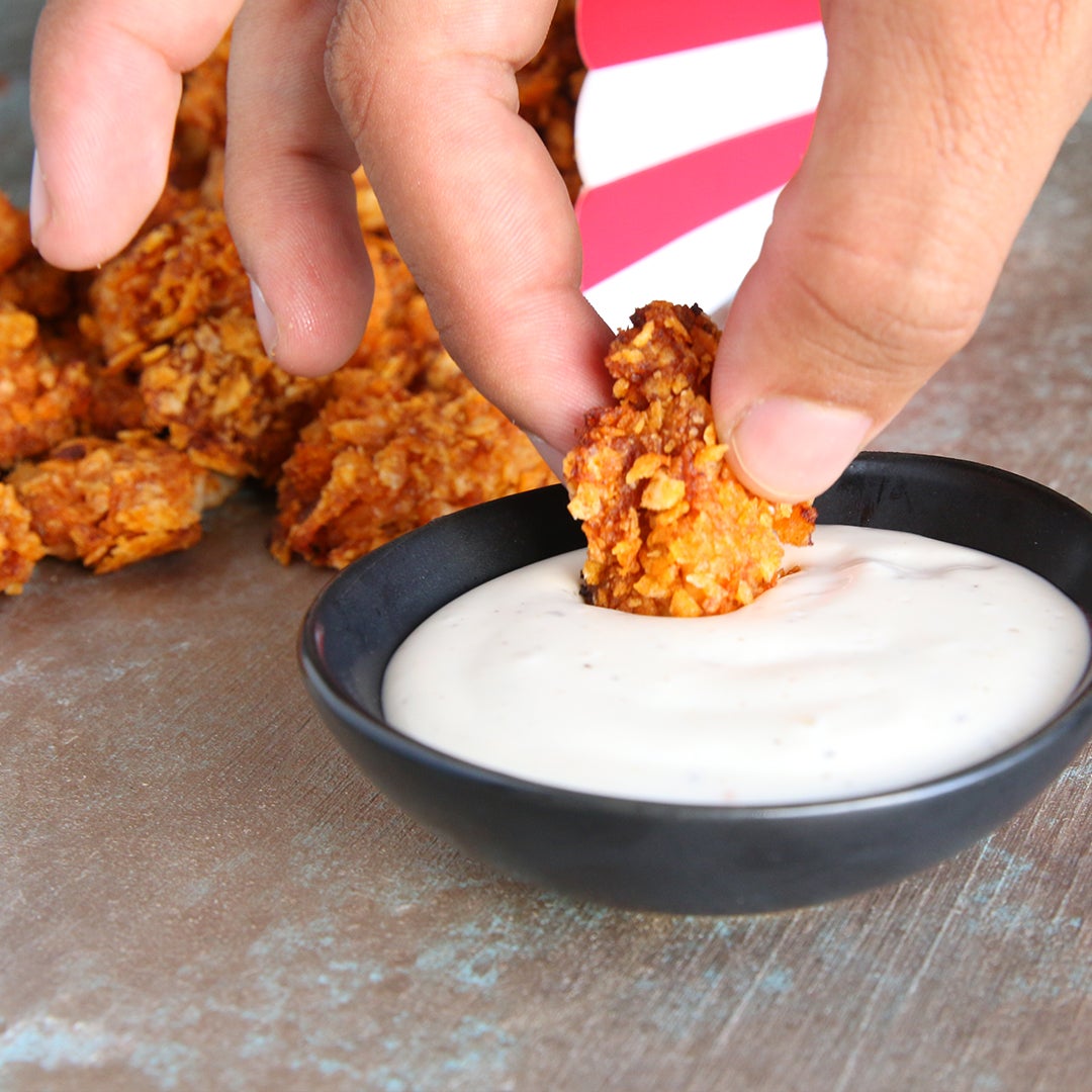 recipes Hand dipping crispy fried chicken into a bowl of creamy white dipping sauce on a textured surface