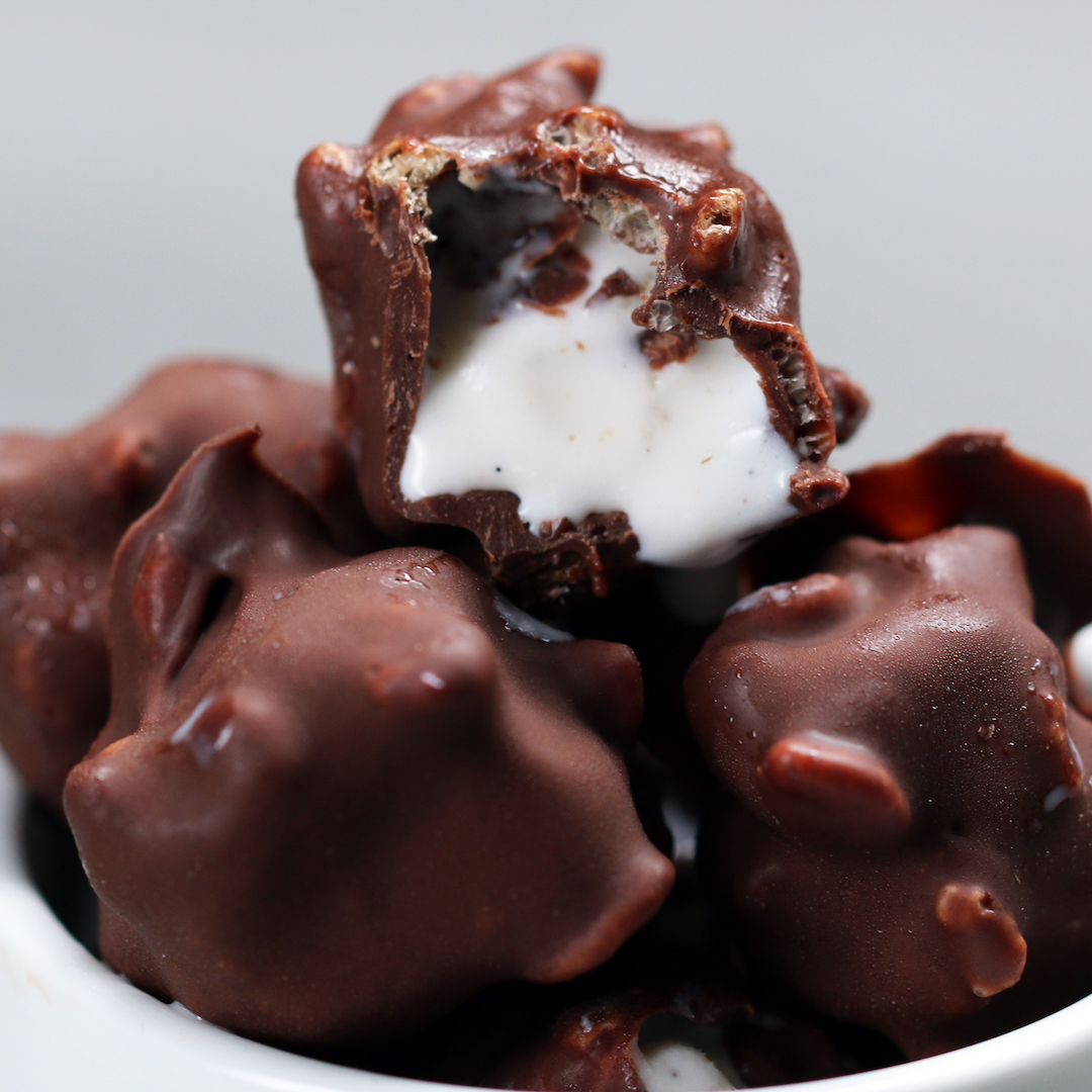 Close-up of chocolate-covered marshmallow bites in a white dish, showcasing a gooey marshmallow center