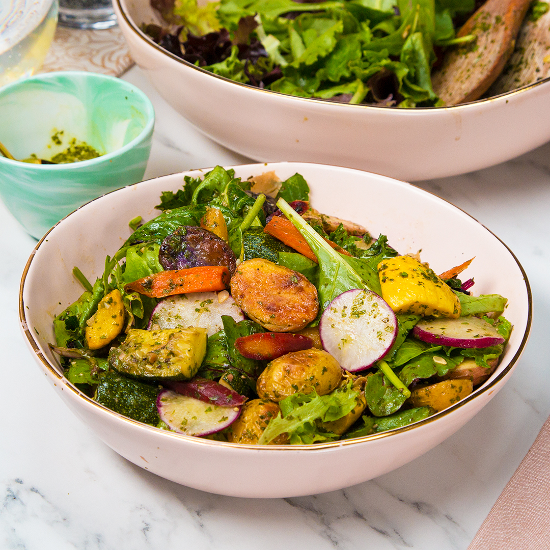 A bowl of fresh salad with radishes, carrots, zucchini, and greens, garnished with herbs