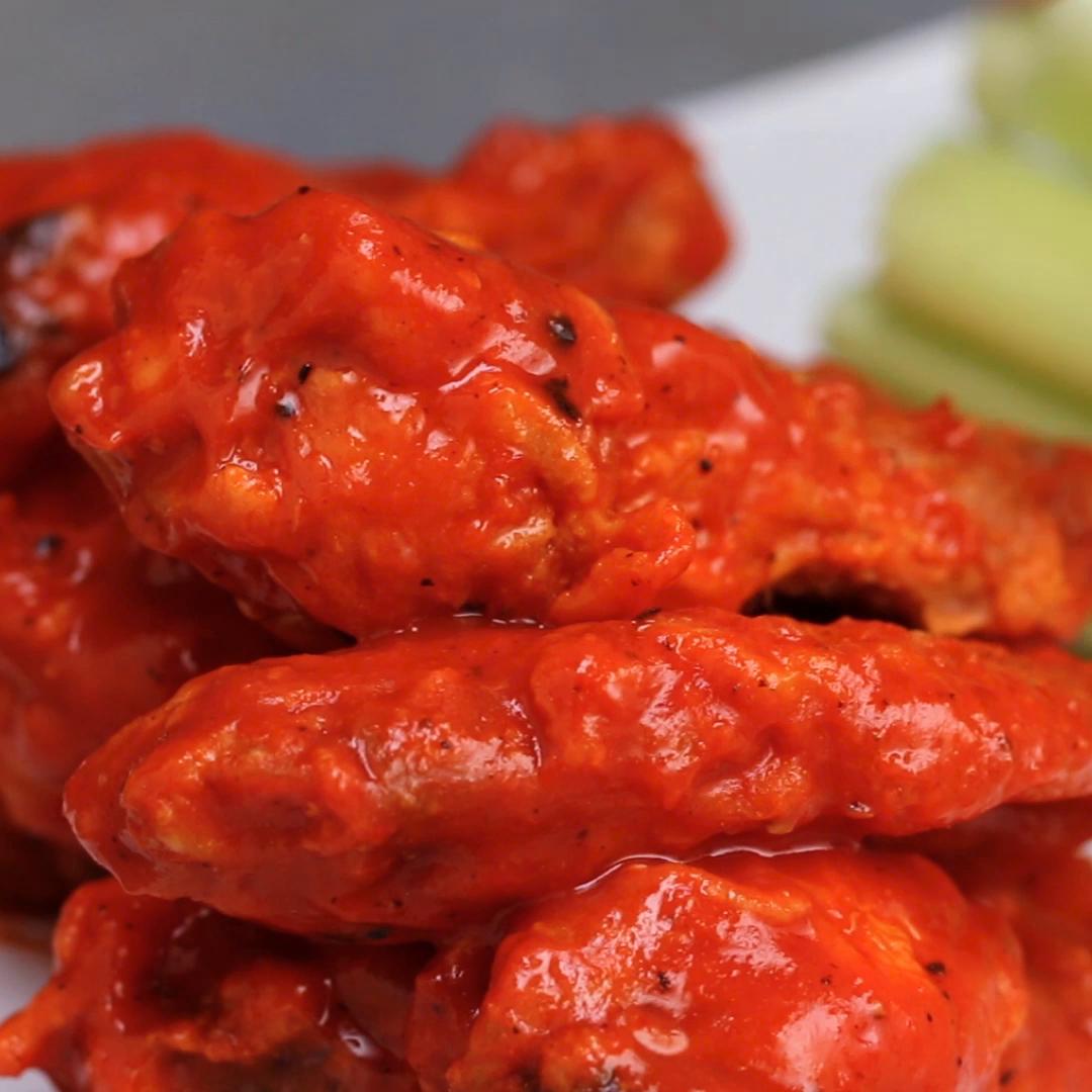 recipes Buffalo chicken wings stacked on a plate, coated in a glossy sauce, with celery sticks in the background