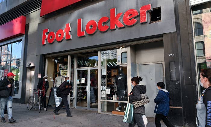 People wearing protective masks walk past a Foot Locker store