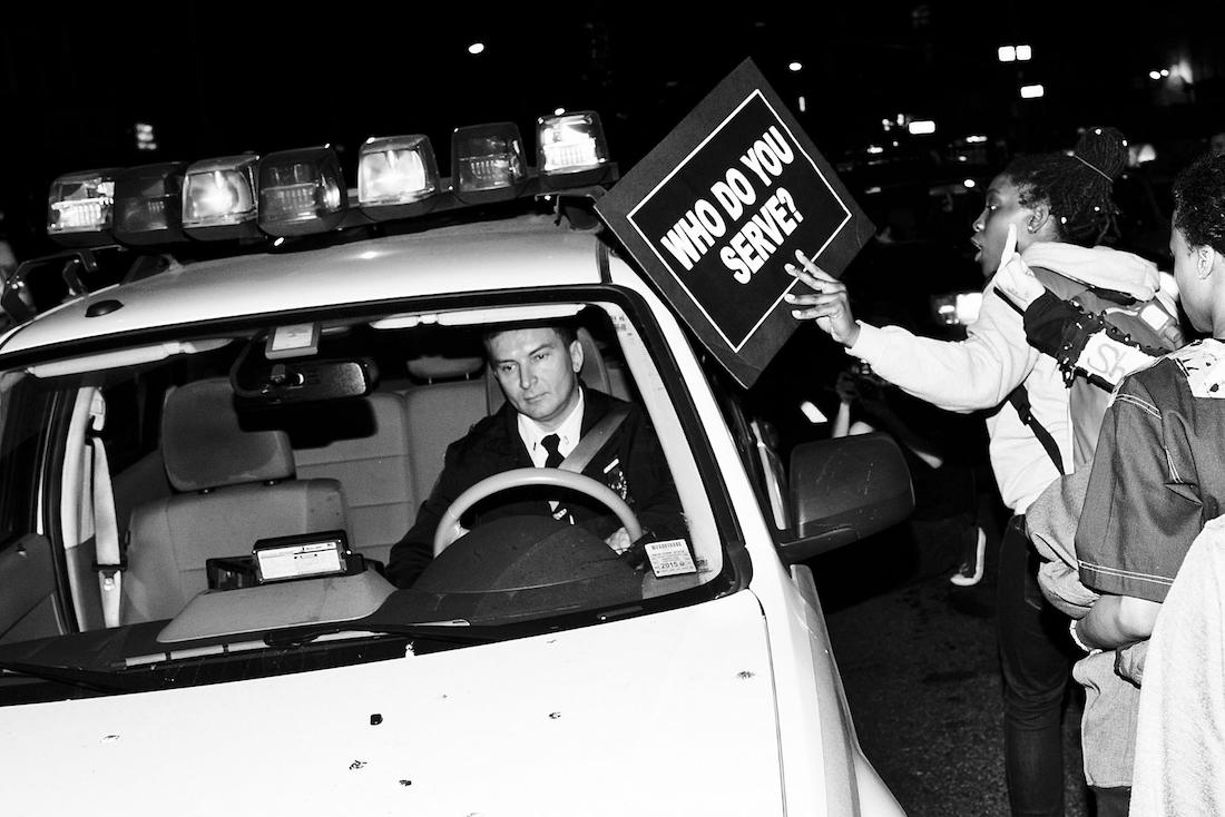 A woman protestor holds a sign up to a police car in New York.