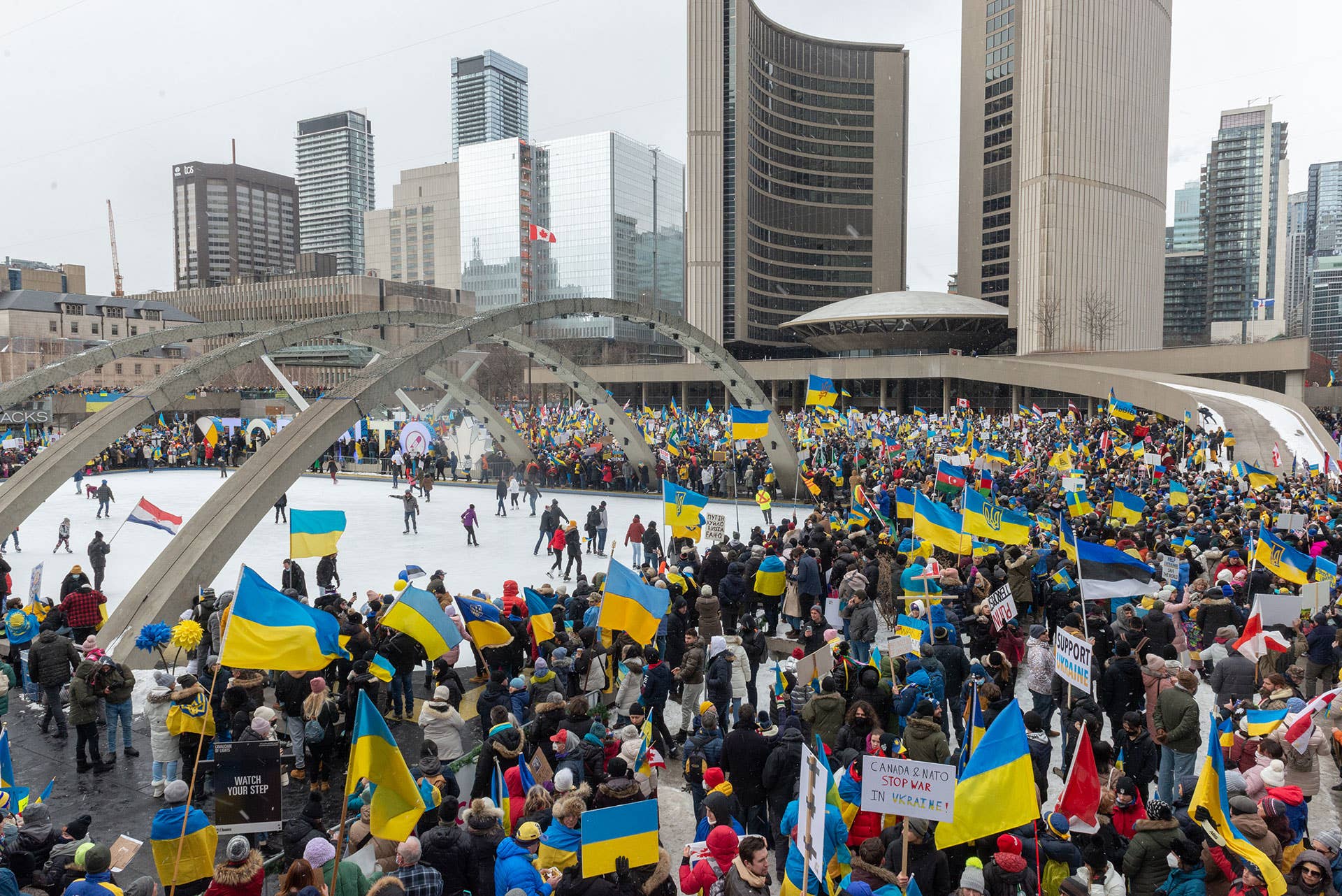 Demonstrators with yellow and blue Ukraine flags and anti-war signs in Downtown Nathan Phillips Square