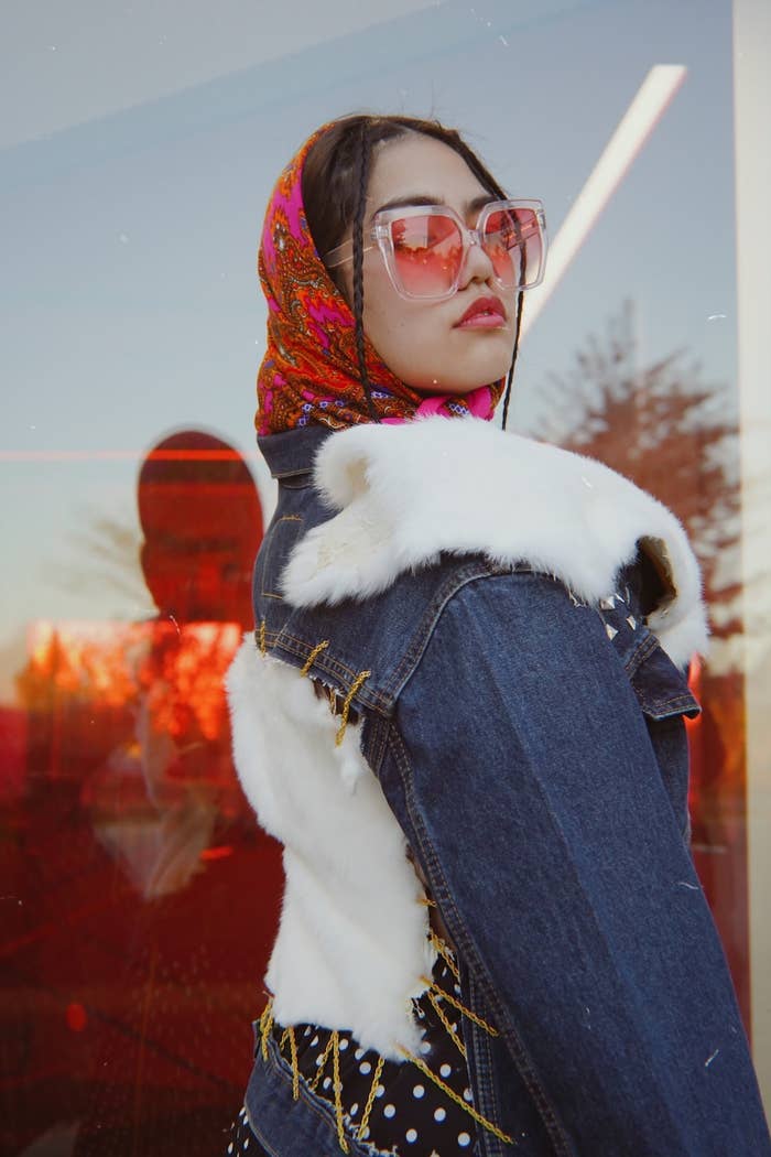 A model wearing a pink paisley headscarf, pink sunglasses, and a jean jacket with white fur attatched