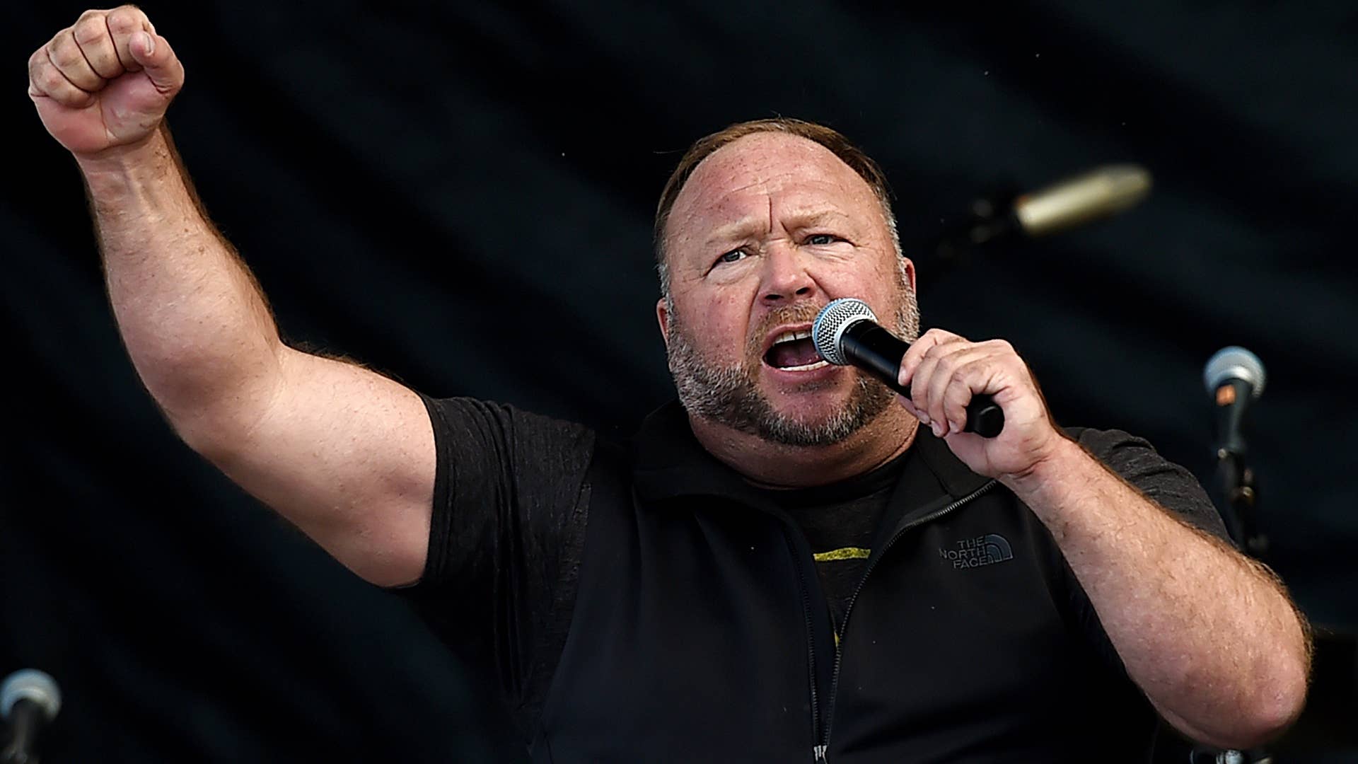 Alex Jones is pictured screaming and holding up a fist