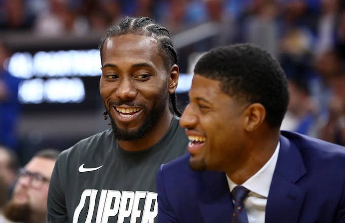 Kawhi Leonard and Paul George smile while sitting on the bench during their game.