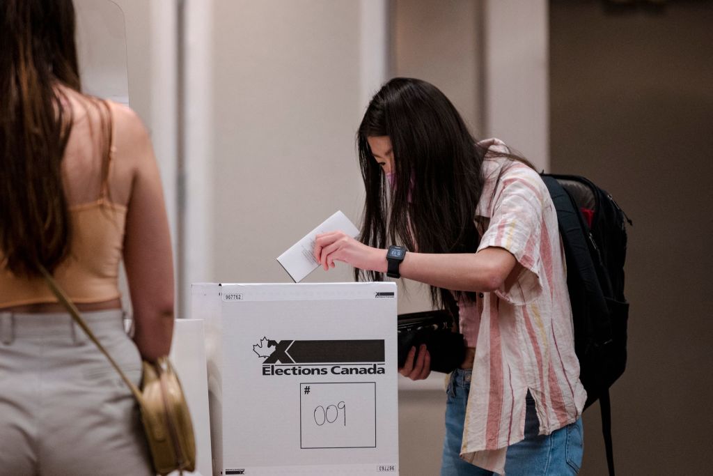 A woma with long black hair placing her ballot in a voting box