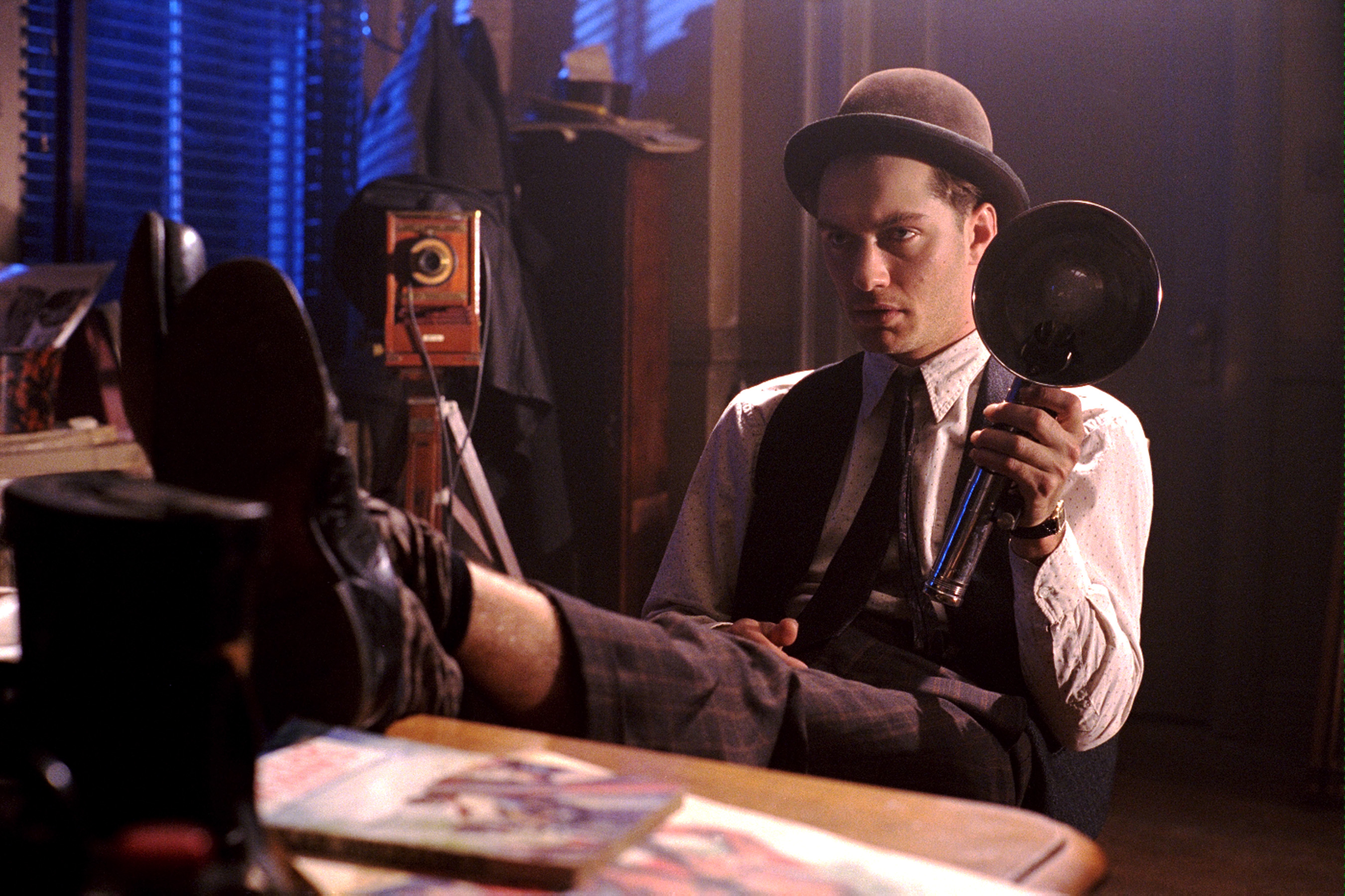 A man in a bowling hat rests his legs on a desk.