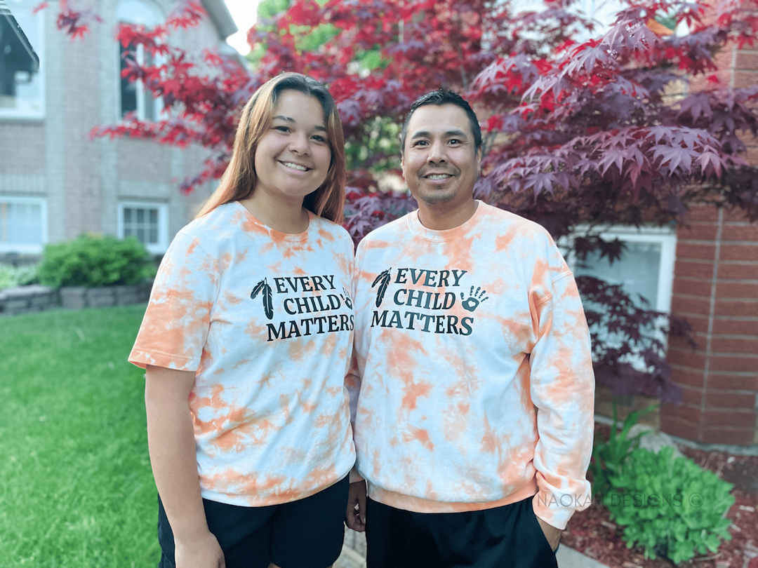 Two people wearing tie dyed orange Every Child Matters shirts from Naokah Designs