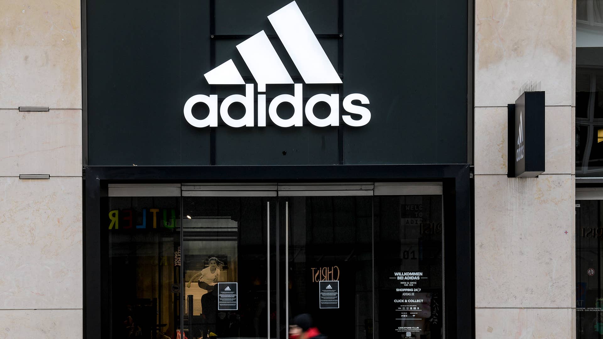 A woman is walking in front of the closed entrance of a department store of the sporting goods manufacturer adidas in downtown Hamburg