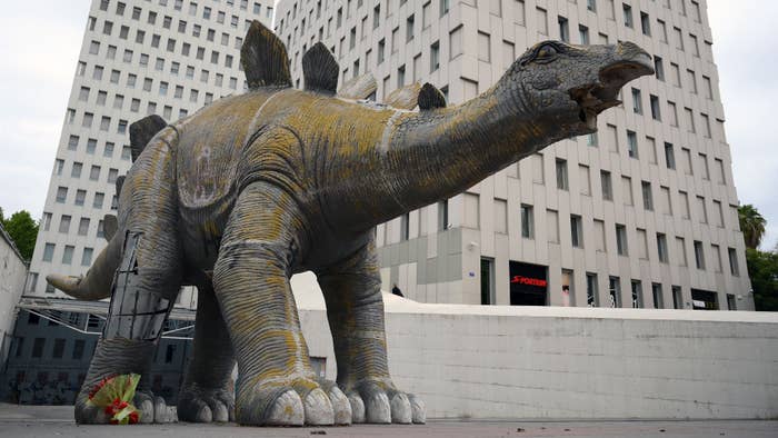 Flowers are placed near a large statue of a dinosaur in Santa Coloma de Gramanet.