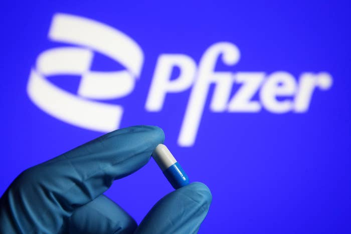 In this photo illustration, a medicine pill is seen in a hand dressed in a medical glove with a Pfizer logo in the background.