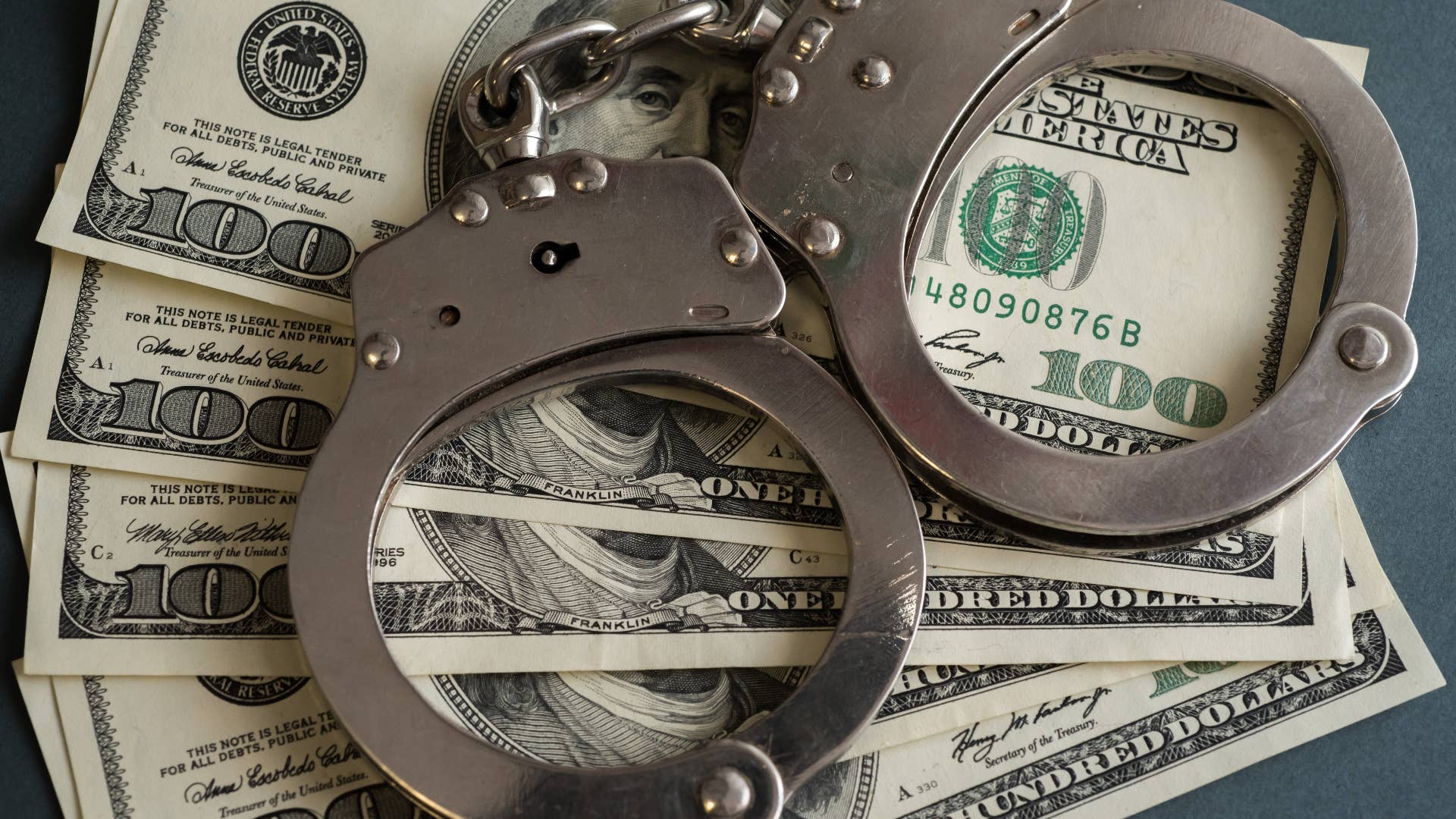 In this photo illustrations handcuffs and hundred us dollar banknotes seen displayed.