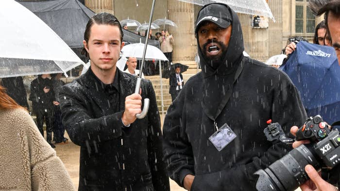 Ye is seen having an umbrella held over him in the rain