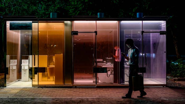 A man walks past a transparent toilet designed by Shigeru Ban.