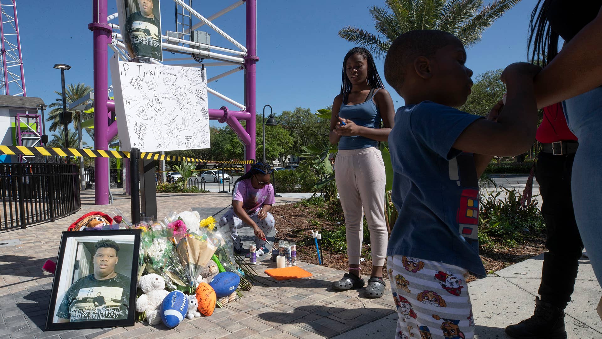 Visitors stand next to the memorial while a family member lights candles for Tyre Sampson, 14