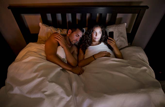 Young couple. Wife on phone while husband is sleeping.