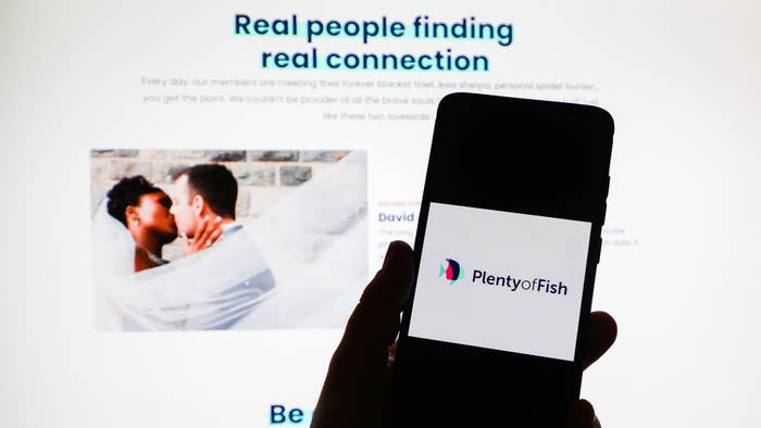 Plenty of Fish app logo is displayed on a mobile phone screen photographed on Plenty of Fish website background.