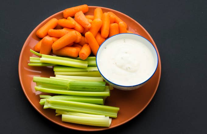 Baby carrots, celery sticks and a bowl full of delicious ranch sauce placed in a brown plate.