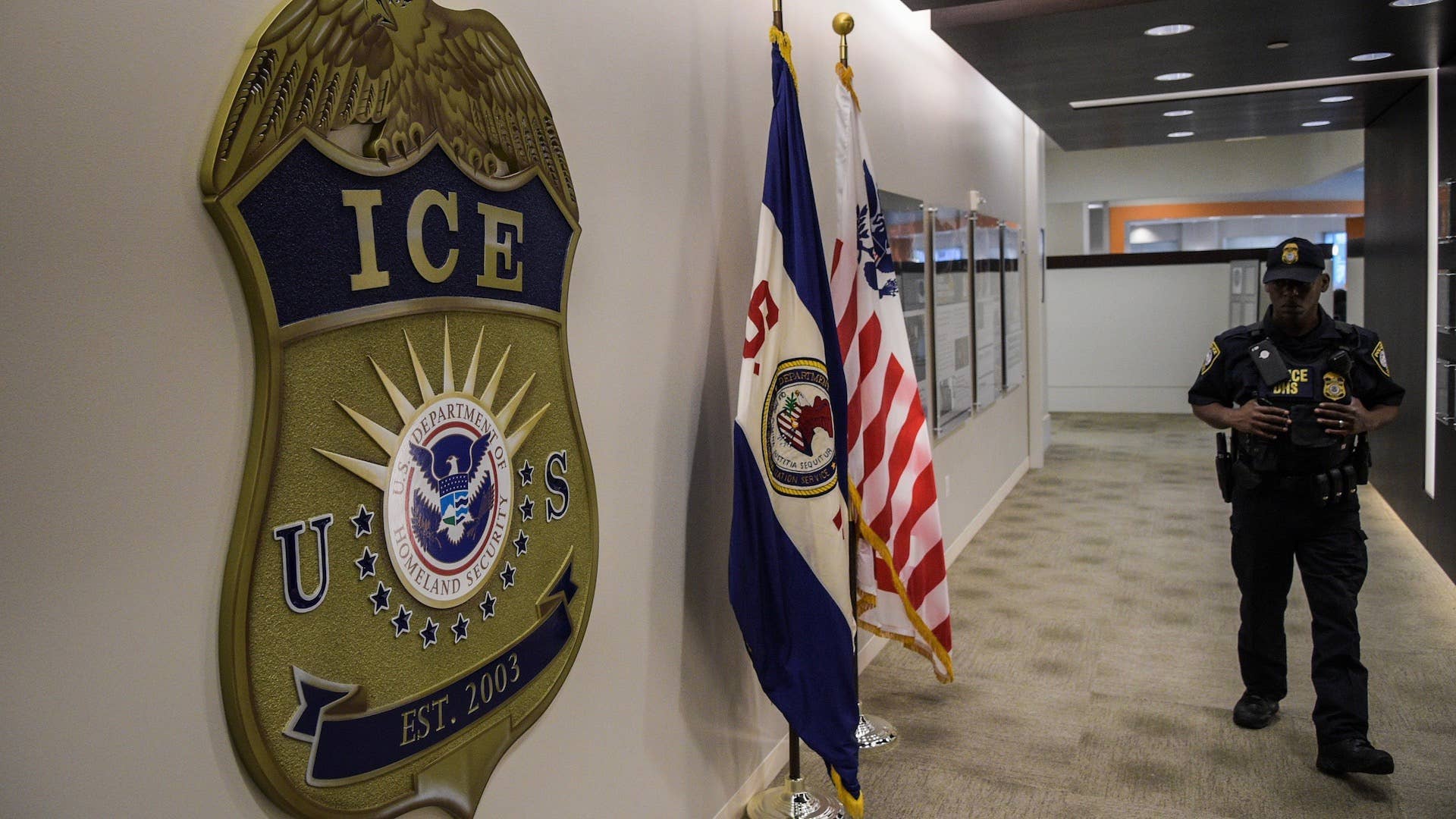 A law enforcement officer walks past ICE logo