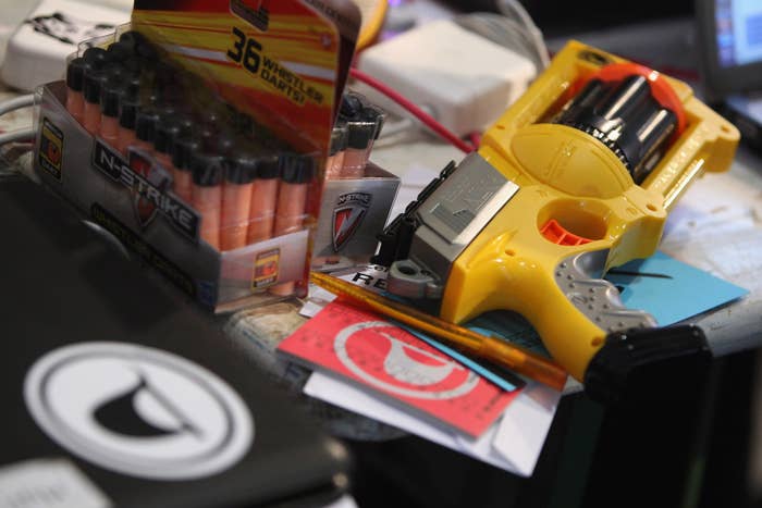 A Pirate Party logo sticker is seen on a laptop next to a Nerf toy dart gun lying on a table.