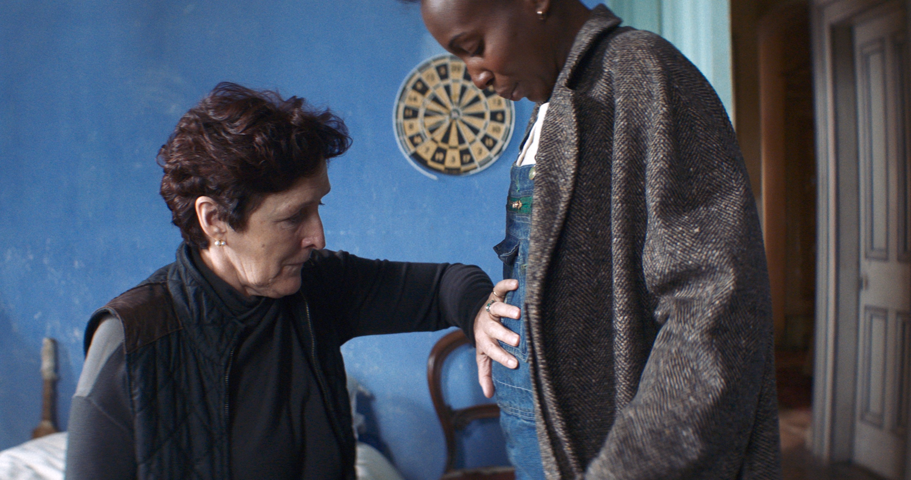 Two women stand in a bedroom.