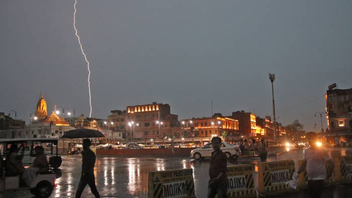 Commuters crosses a road as it rains during a lightning strike in the sky in Jaipur, Rajasthan, India.