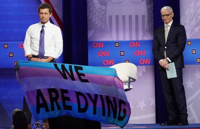 Pete Buttigieg and Anderson Cooper react as protestors display banners.