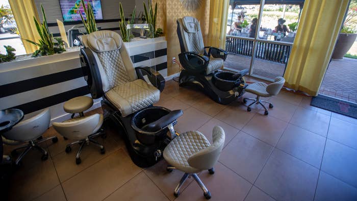 Inside chairs are empty as beauty technicians wear face masks while giving clients wearing face masks manicures and pedicures outdoors.