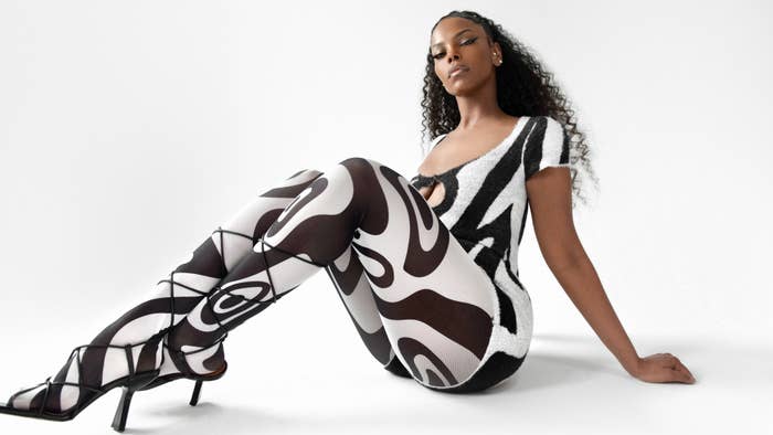 Amaal wearing a black and white geometric outfit, with black heels, sitting