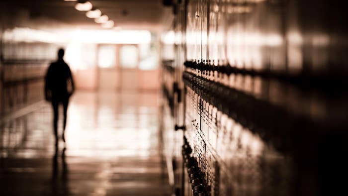 A high school student walks down a dark hallway in a public high school,