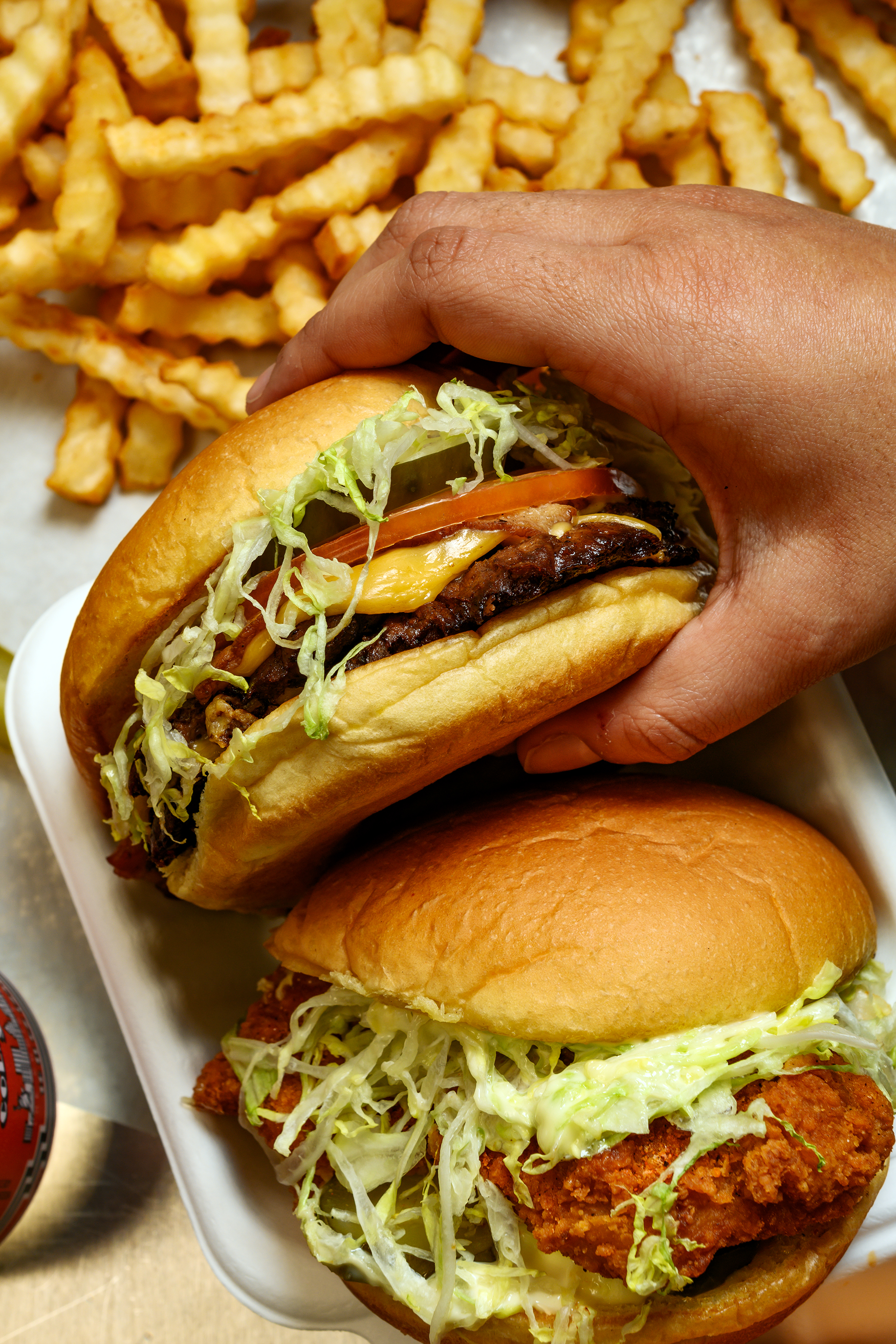 A hand holding a burger over fries