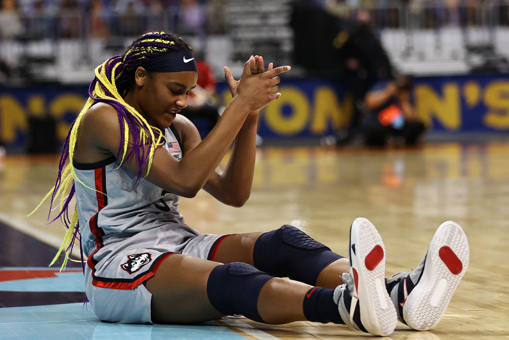 Aaliyah Edwards sitting on the floor of a basketball court in a Huskies uniform